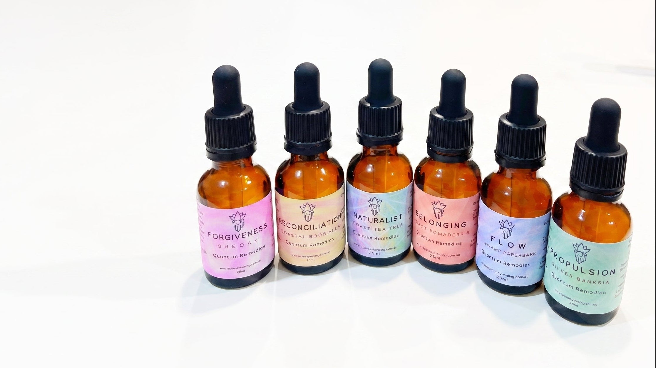 Six Quantum Remedies in small amber glass dropper bottles with black caps and pastel-colored labels, arranged in a row on a white background.